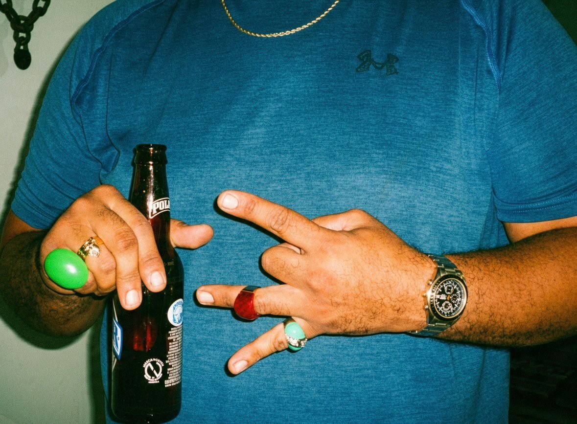 Hands with green, red and turquoise rings holding a Polar beer and throwing a hand sign.